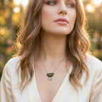Woman wearing Evergreen Necklace by Jillery outdoors with a 14K yellow gold dainty chain and a custom yellow gold pendant featuring a green tourmaline and a blue topaz 