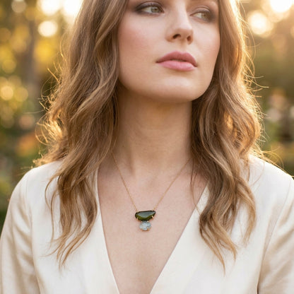 Woman wearing Evergreen Necklace by Jillery outdoors with a 14K yellow gold dainty chain and a custom yellow gold pendant featuring a green tourmaline and a blue topaz 