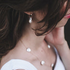 Close-up of a person wearing baroque pearl huggie hoop earrings and a necklace with a blurred background
