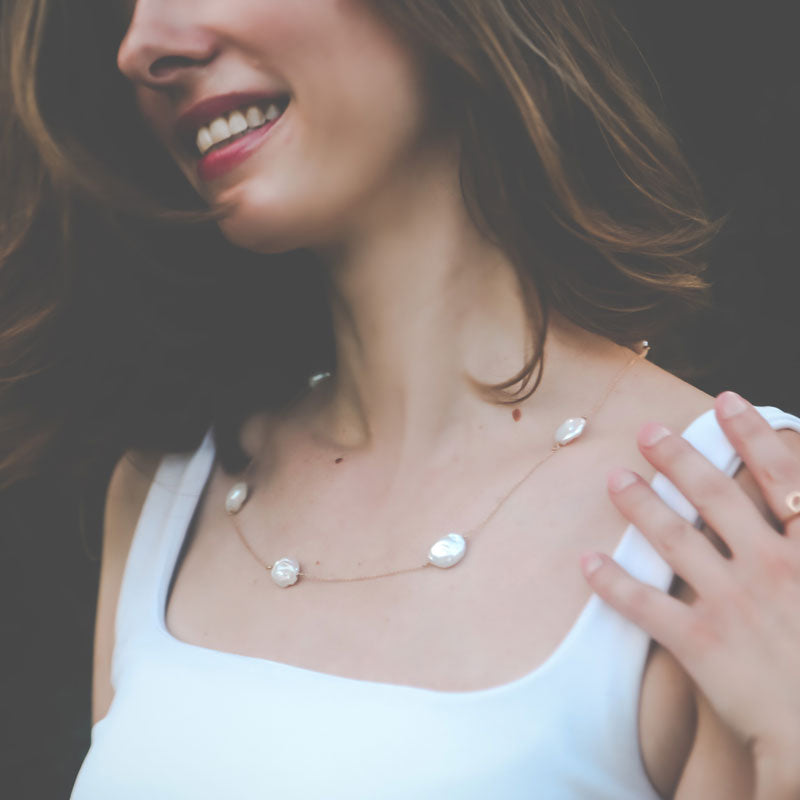 Woman wearing a delicate necklace with keshi pearl stones stationed on a yellow gold chain against a blurred background
