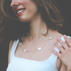 Woman wearing a delicate necklace with keshi pearl stones stationed on a yellow gold chain against a blurred background