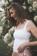 Woman wearing a white tank top and haven keshi pearl station necklace in 14K yellow gold with a blurred floral background