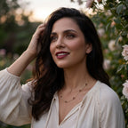 Kindred Necklace worn by woman wearing soft silky cream colored bluse outside at golden hour. The necklace features bezel set pear cut Mozambique Garnets stationed on a delicate yellow gold chain
