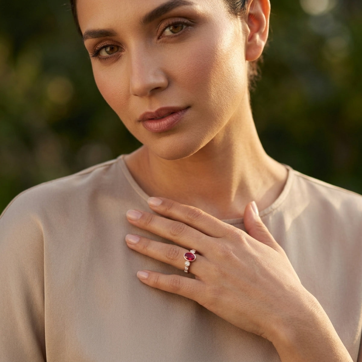 Woman wearing a ring with a pinkish red gemstone, standing outdoors with a blurred green background