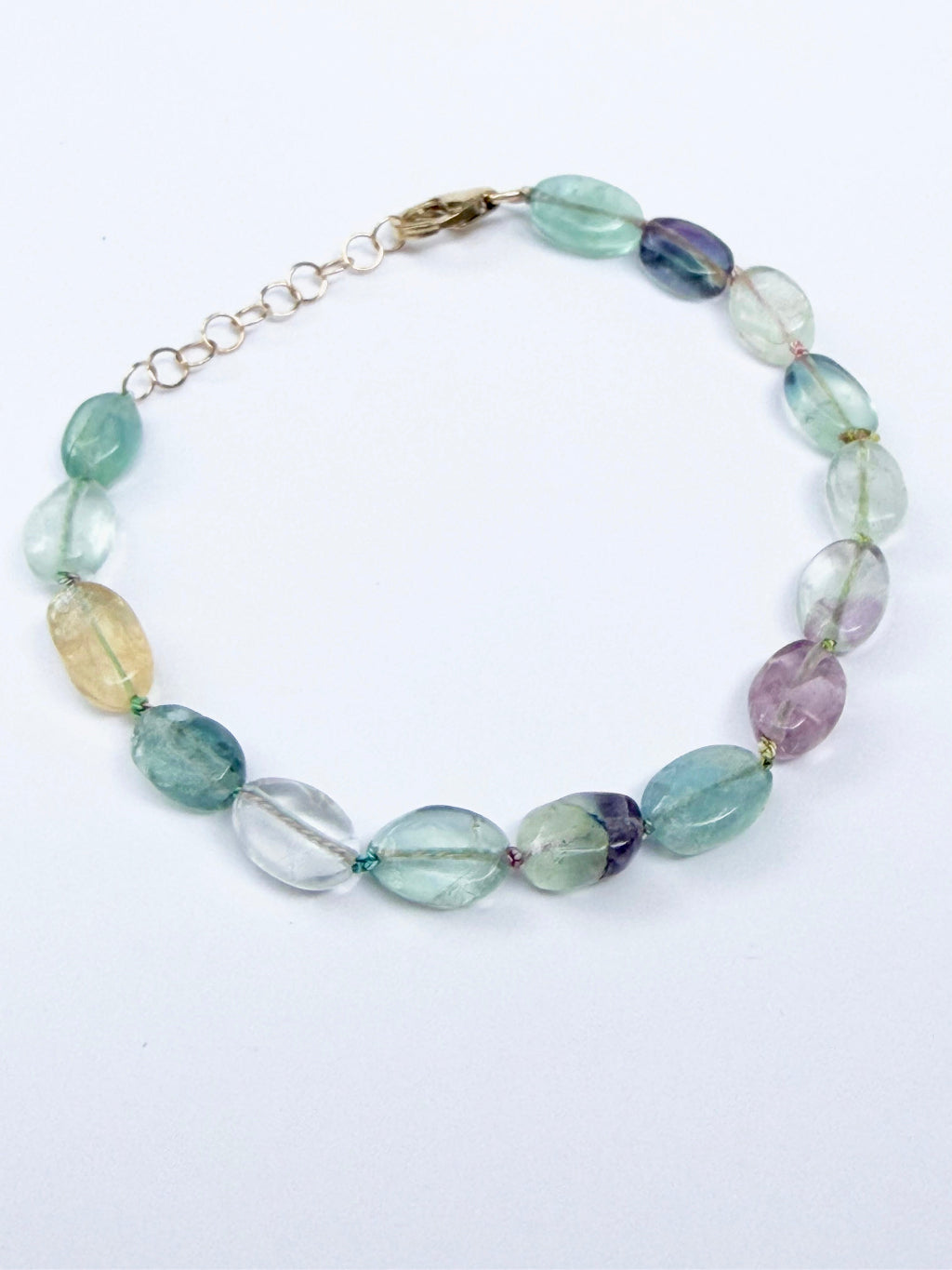 A beaded gemstone bracelet with oval faceted beads in shades of light green, aqua, lavender, and pale yellow, connected by a gold-tone chain extender.