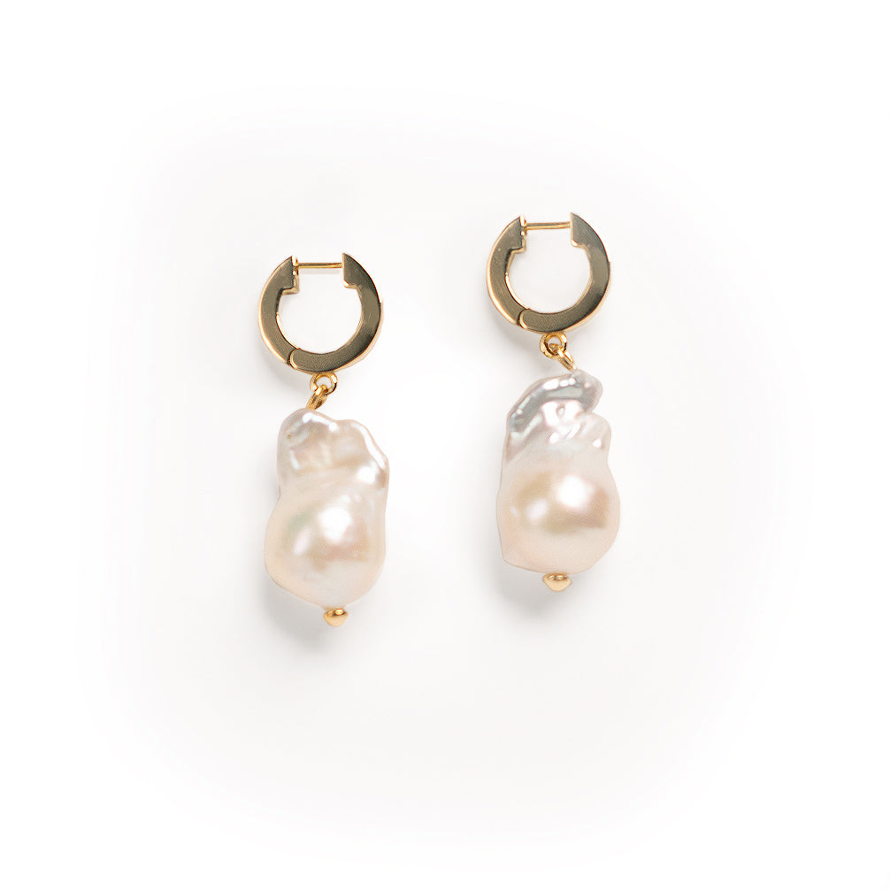 Pair of baroque pearl dangle earrings with gold huggie hoop components on a white background