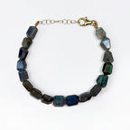 A beaded bracelet made of faceted dark blue and gray labradorite stones, connected by a gold-tone chain extender and lobster clasp, shown on a plain white background.