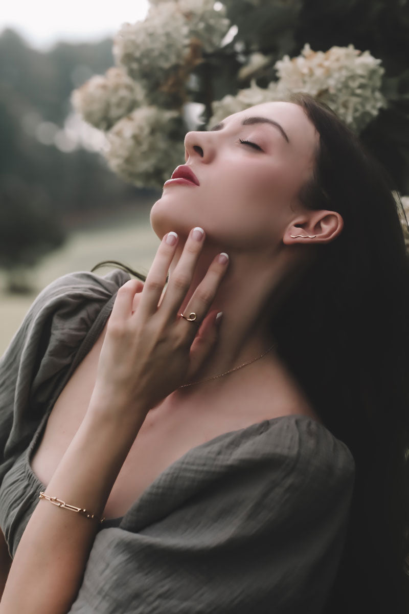 Woman in a natural setting with flowers and greenery wearing squiggle ear climber, flow ring and lines and dots bracelet