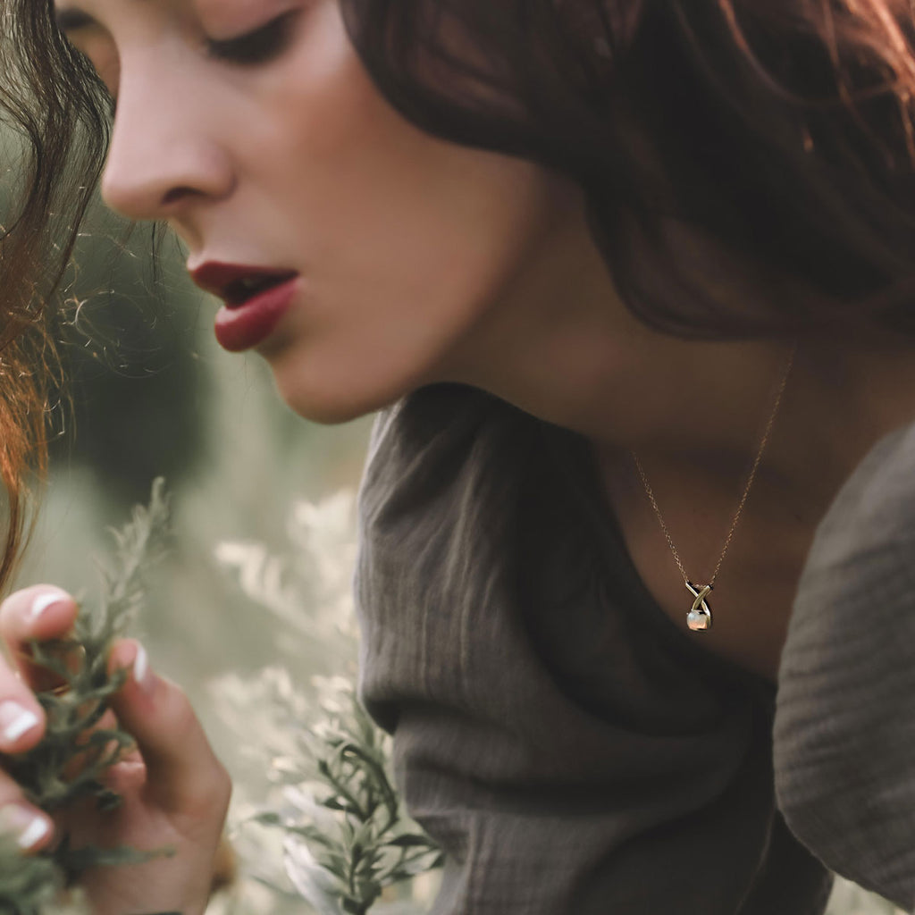 woman wearing 14k yellow gold loopy ethiopian opal necklace holding a pine tree branch in a forest setting