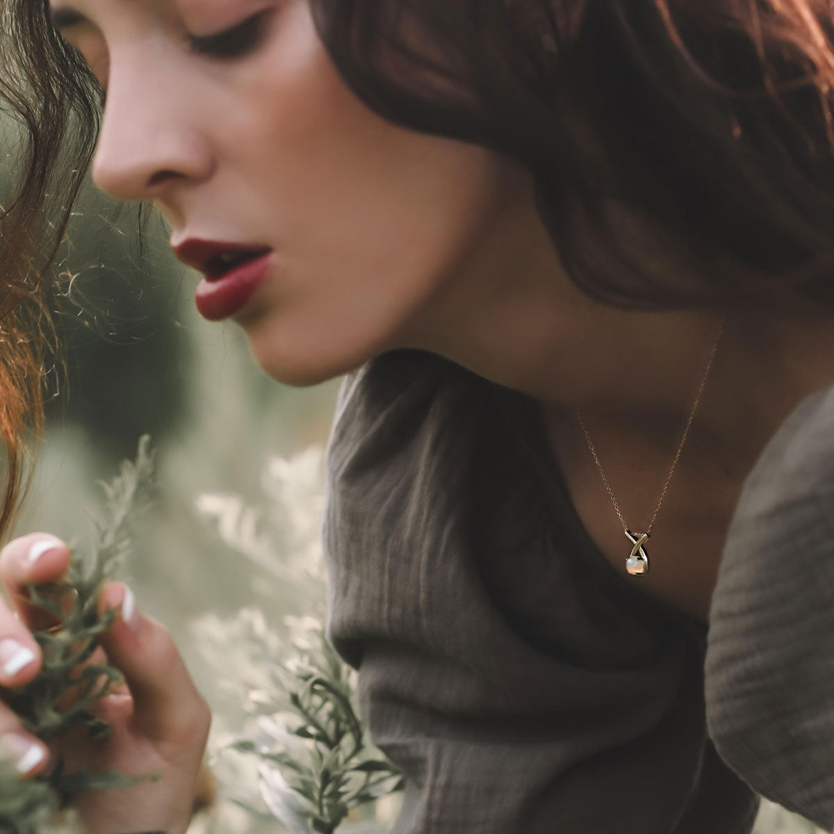 woman wearing 14k yellow gold loopy ethiopian opal necklace holding a pine tree branch in a forest setting