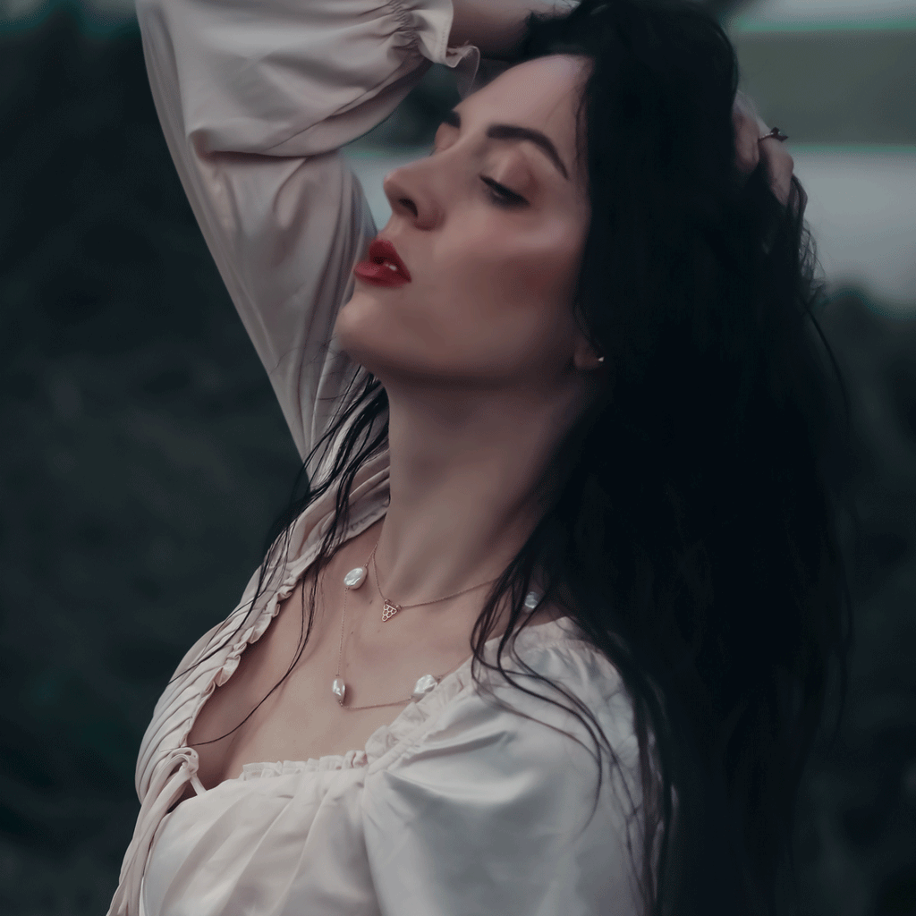 haven station necklace and fish scales necklace worn by model with red lip, black wispy hair and silk off white blouse near dusk in an outdoor setting