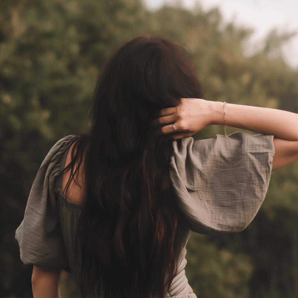 womans back with arm elevated adn showing lines and dots bracelet and flow ring in 14K yellow gold in outdoor setting near golden hour