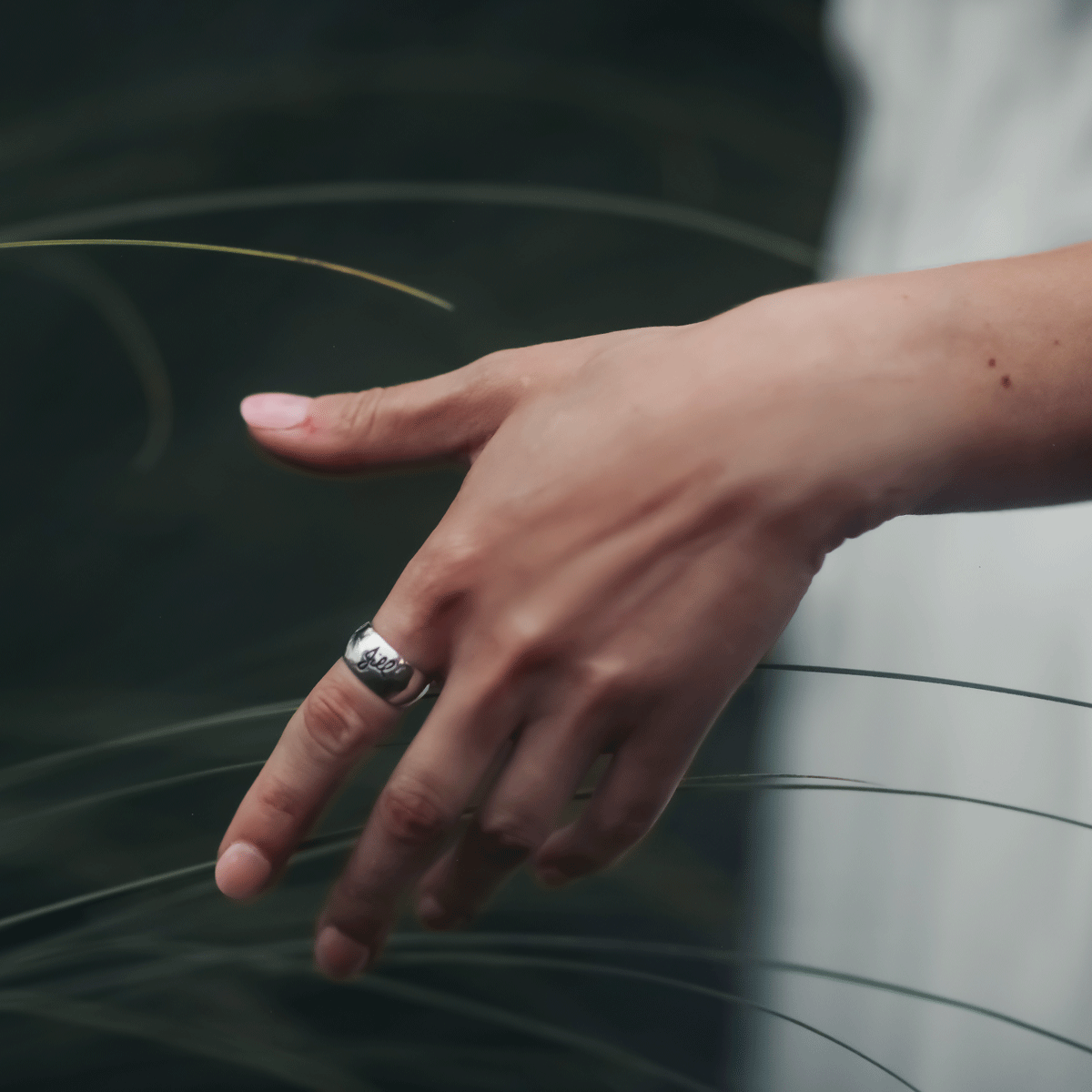 personalized band with custom signature and blackening finish inside hand drawn signature on a high polished wide white gold cigar band worn on hand brushing seagrass in natural setting