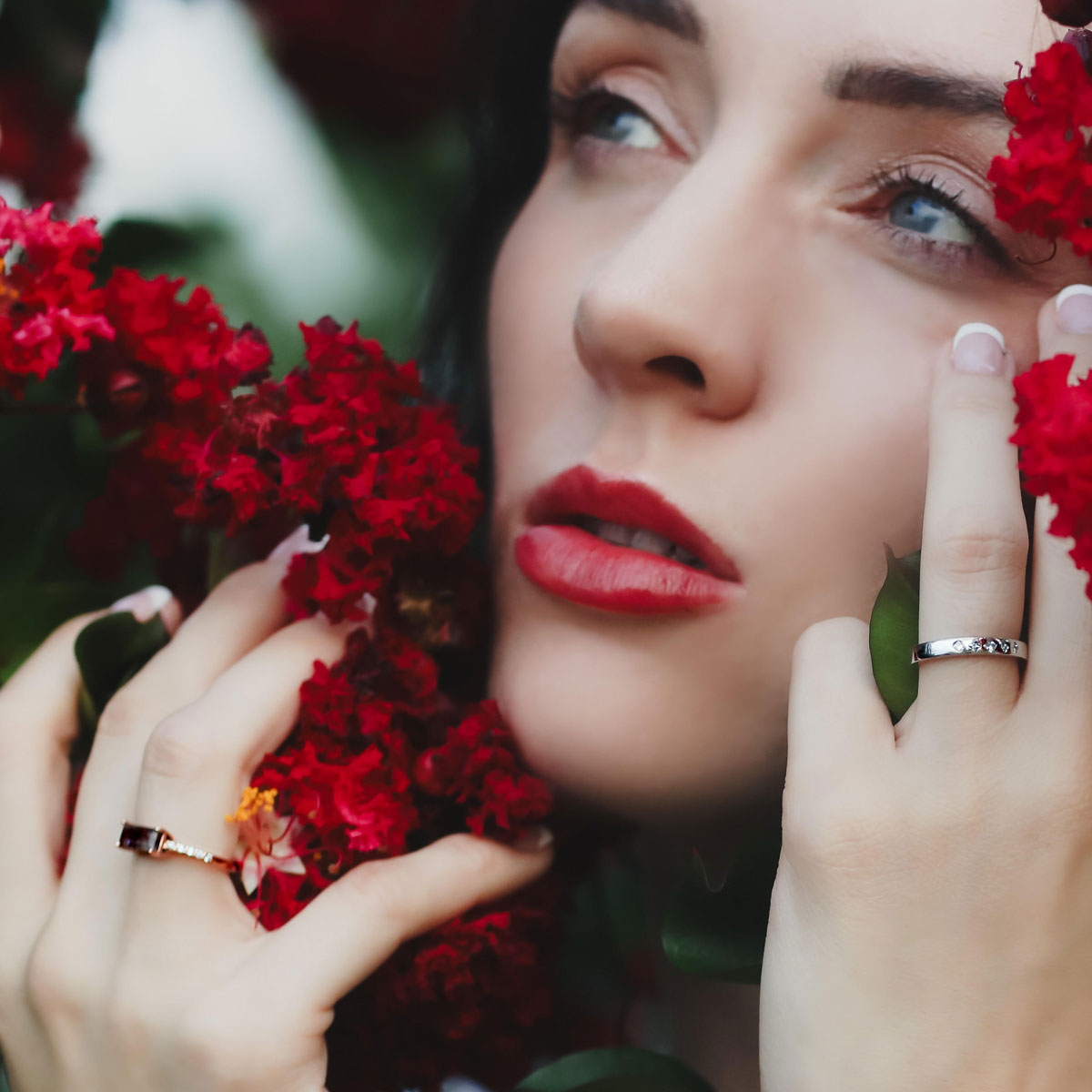Woman with red lipstick holding red flowers and wearing 14k rose gold cacoxenite diamond ring against a blurred natural background