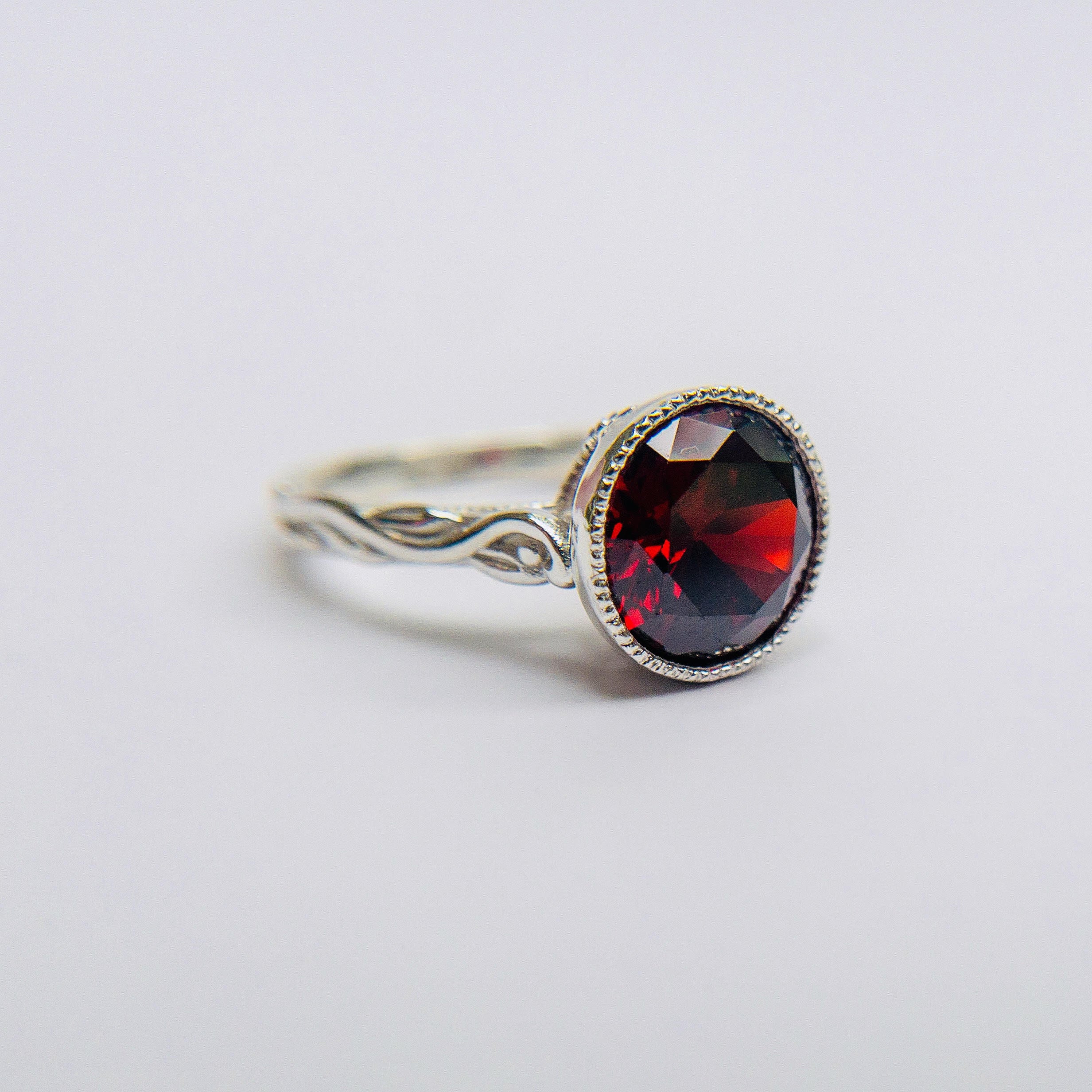 Silver ring with a red garnet gemstone on a light gray background